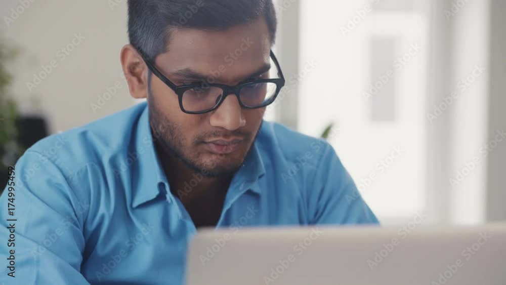 Close-up of a man wearing a blue shirt in glasses uses a laptop, smiling. Manager, marketing, business, communication, work. In the office. Shot on RED Epic Camera.