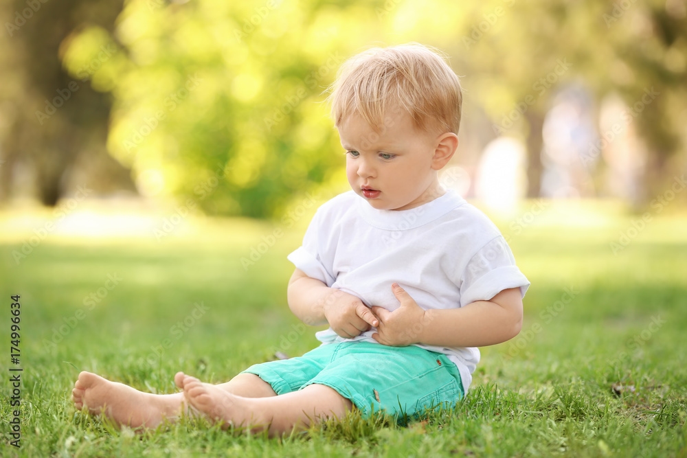 Cute baby boy sitting on green grass in park Cute baby boy sitting on green grass in park