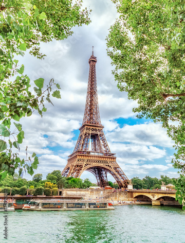 Classic view on Eiffel Tower through green poplar foliage over Seine river in Paris. Beautiful summer morning scenery. Vertical orientation. Eiffel Tower is famous travel destination in Europe. © Feel good studio