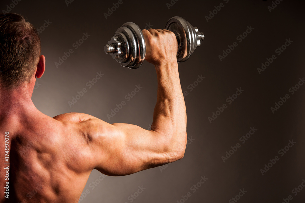 Strong male athlete works out with dumbbells in studio over dark backgound Strong male athlete works out with dumbbells in studio over dark backgound