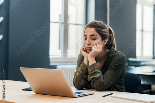 Portrait of young bored attractive female student looking at laptop.