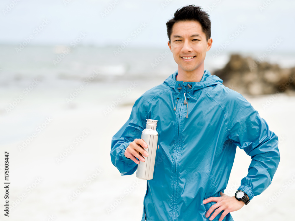 Young man in sport clothes drinking water after workout on the beach Young man in sport clothes drinking water after workout on the beach