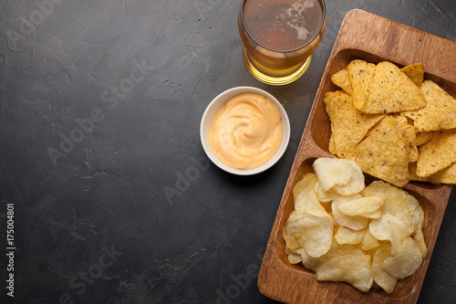 Beer in glasses closeup on the concrete table. Beer and snacks are chips and nachos in wooden bowl with cheese souce. top view. Copy space. Drink and snack for the football match or party photo