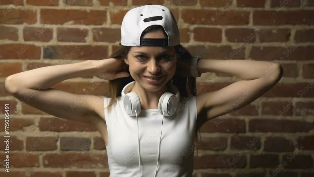 Caucasian hipster girl, with white headphones around her neck, touching her hair before the brick wall, isolated, slow motion Caucasian hipster girl, with white headphones around her neck, touching her hair before the brick wall, isolated, slow motion