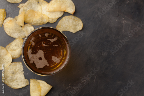 Close-up cold beer in a long glass and of potato chips on a dark stone with copy space. Top view