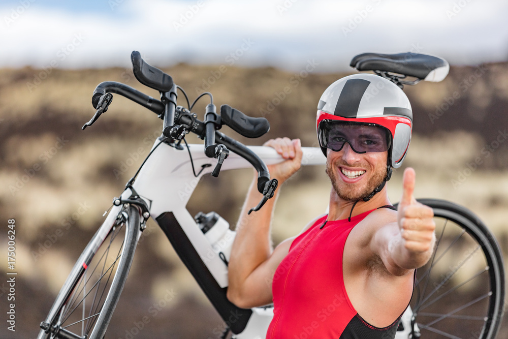 Naklejka premium Triathlon biking - male triathlete cycling giving thumbs up success hand sign cheering happy excited at camera. Fit man cyclist on professional triathlon bicycle for ironman race. Big Island, Hawaii.
