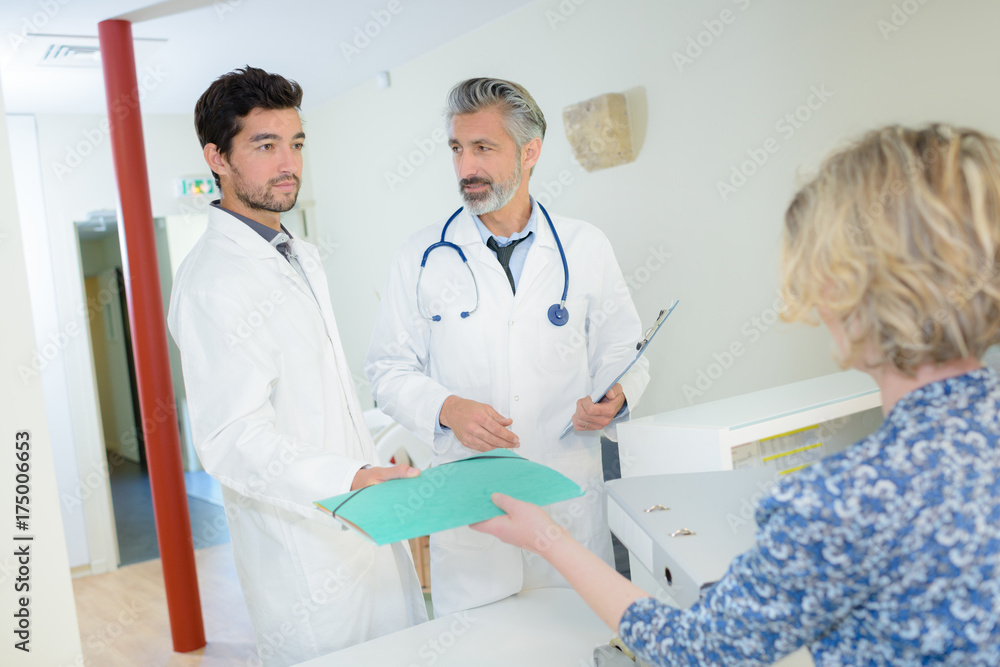 woman behind the reception desk giving folder to doctors woman behind the reception desk giving folder to doctors