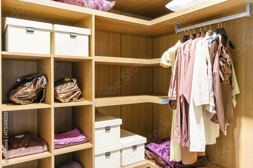 modern wooden wardrobe with clothes hanging on rail in walk in closet design interior