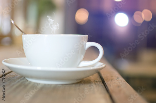 White cup with steaming hot coffee on wooden table with bokeh background at cafe