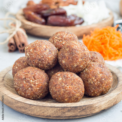 Healthy homemade paleo energy balls with carrot, nuts, dates and coconut flakes, on a wooden plate, square format