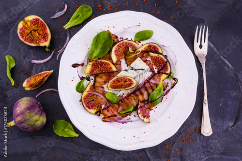 Figs and fried bacon with small lettuce leaves served on a white plate. Italian food. 