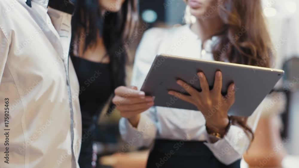 Young Manager woman in glasses talking to a couple. Shows the product using a tablet computer in a modern office. Smiling. Management, meeting. Business. Work. Shot on RED Young Manager woman in glasses talking to a couple. Shows the product using a tablet computer in a modern office. Smiling. Management, meeting. Business. Work. Shot on RED