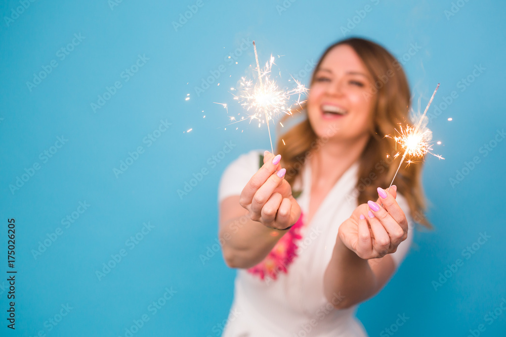 Portrait of a happy woman holding bengal lights over blue background with copy space. Christmas, celebrations and holidays concept Portrait of a happy woman holding bengal lights over blue background with copy space. Christmas, celebrations and holidays concept