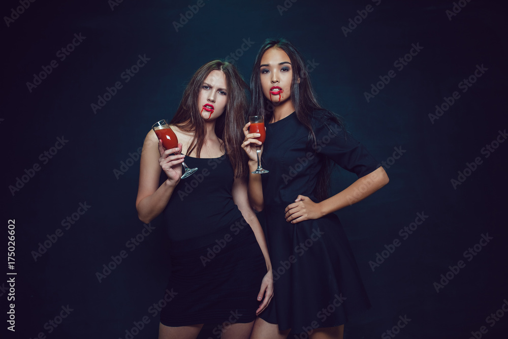 Attractive girls in the image of vampires hold glasses with blood. Halloween. Attractive girls in the image of vampires hold glasses with blood. Halloween.
