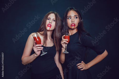 Attractive girls in the image of vampires hold glasses with blood. Halloween.