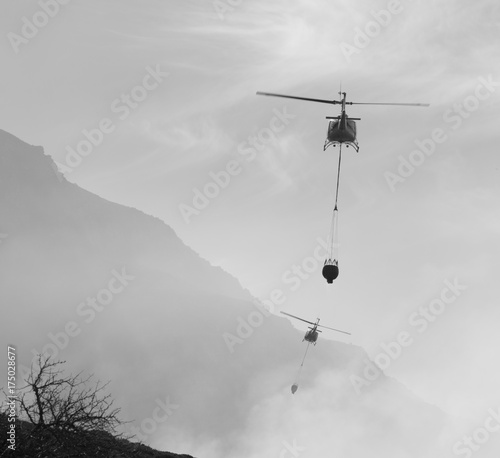 A pair of firefighting helicopters take turns to dump water onto a bush fire in Cape Town, South Africa.