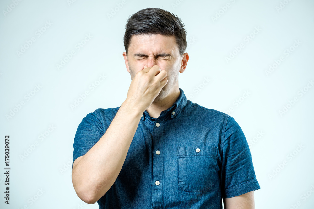 Man holding his nose against a bad smell over gray background Man holding his nose against a bad smell over gray background
