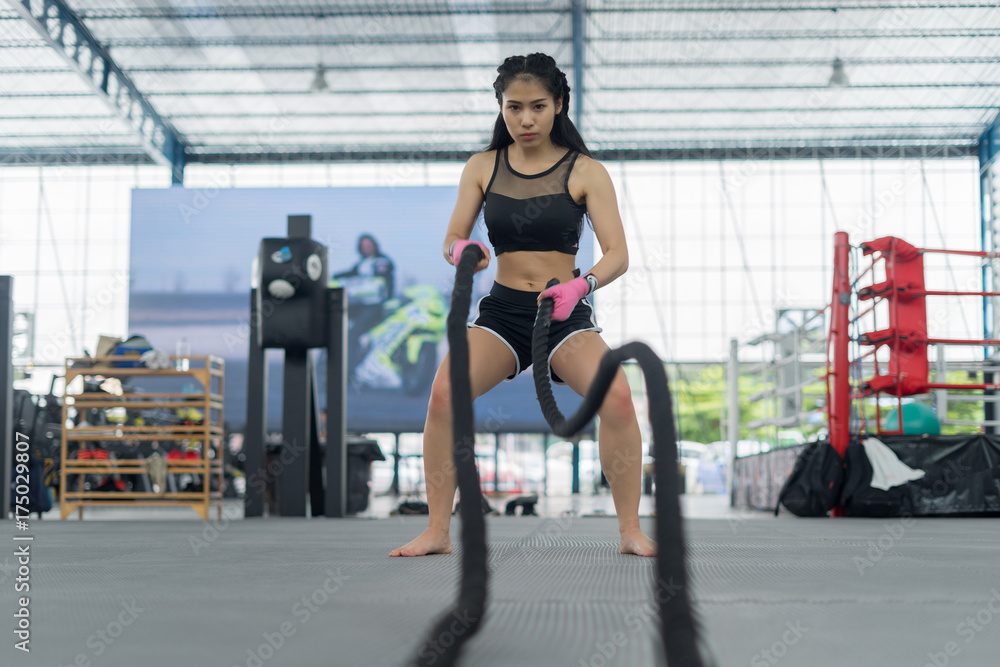 Fitness woman in training showing exercises with battle rope in gym
