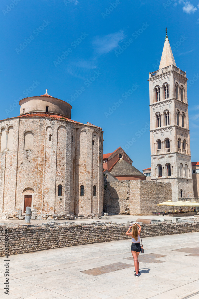 Blond girl is photographing monuments of historic center of the Croatian town of Zadar at the Mediterranean Sea, Europe.