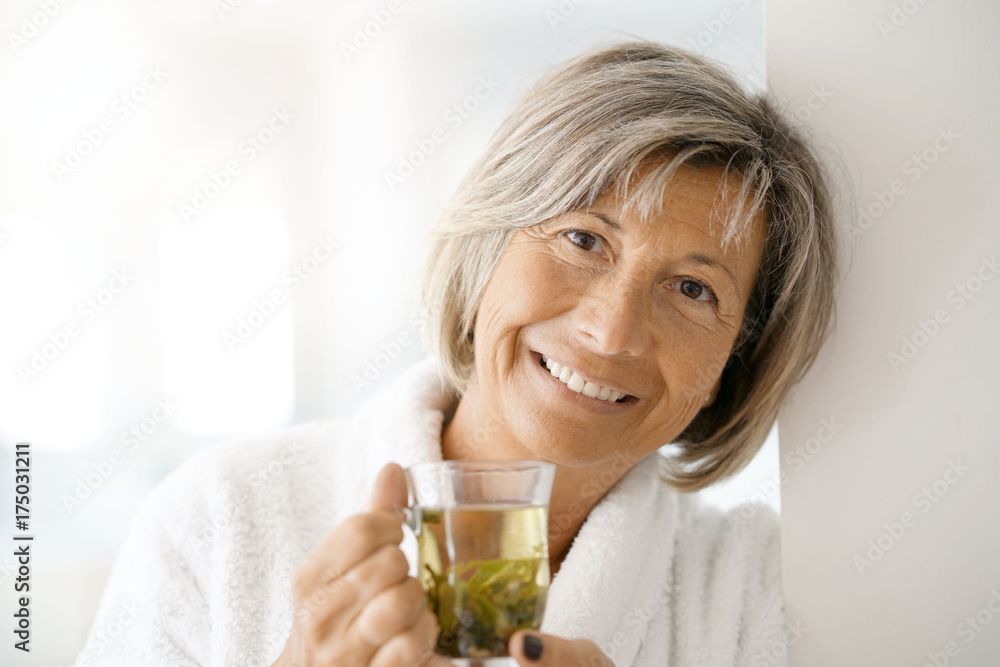 Senior woman in bathrobe drinking hot green tea Senior woman in bathrobe drinking hot green tea