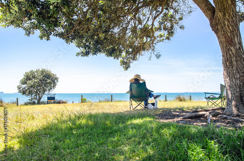 A women sitting under the tree and enjoying the beautiful landscape view of the ocean in New Zealand.