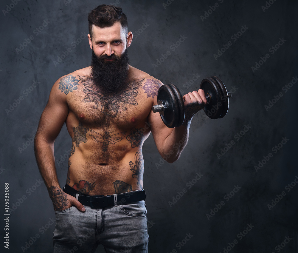 Shirtless muscular, bearded male holds dumbbell.
