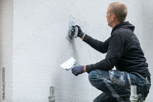 construction worker putting decorative plaster on house exterior photo