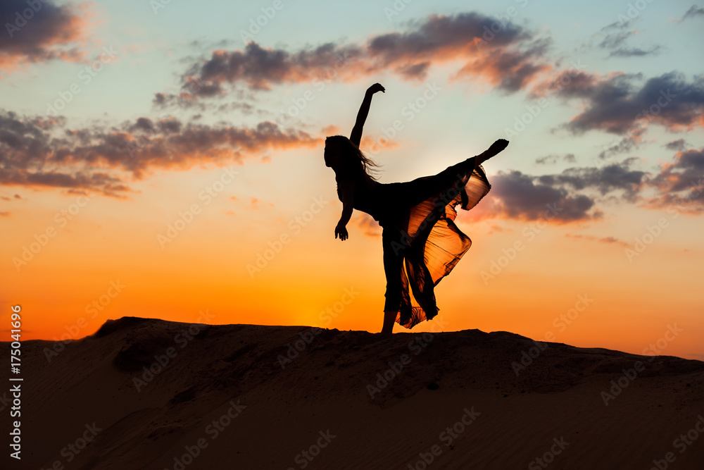Naklejka premium Dancing at night in the sand against the backdrop of the setting sun, the silhouette of a dancer.