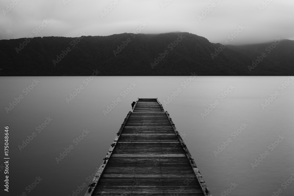 Wooden jetty and flat calm lake, dark low light Wooden jetty and flat calm lake, dark low light