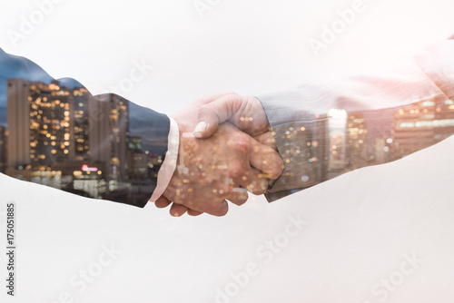 The double exposure image of the business man handshaking with another one during sunrise overlay with cityscape image. The concept of modern life, business, city life and teamwork. photo