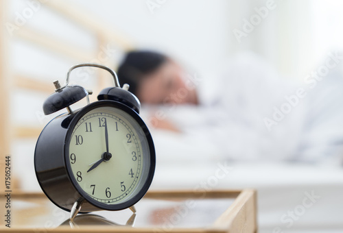 Closeup alarm clock, Young asian woman sleeping on the bed in the early morning and late work time or study