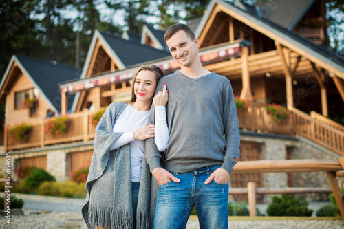 Young attractive married couple standing outside their large wooden cottage in the woods.