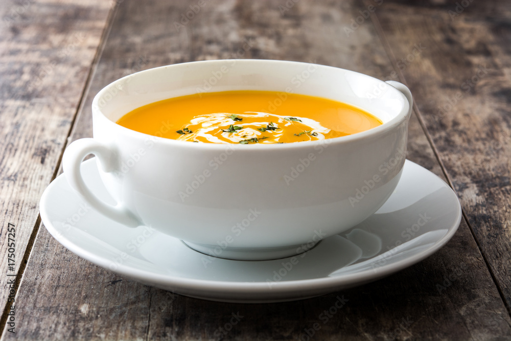Pumpkin soup in white bowl on wooden table