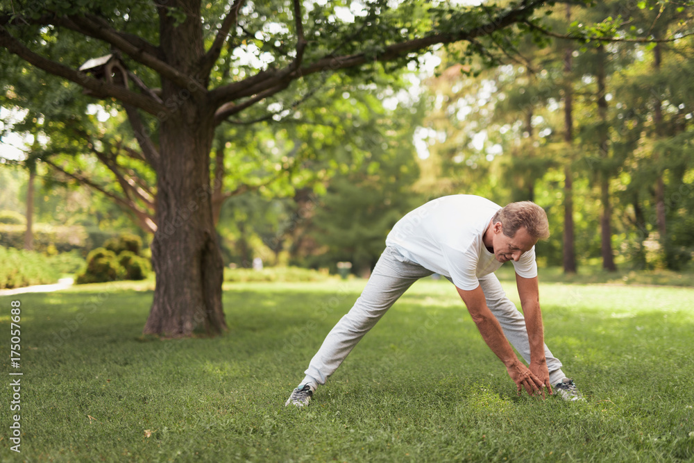 A man in light sportswear is doing exercises in the park A man in light sportswear is doing exercises in the park