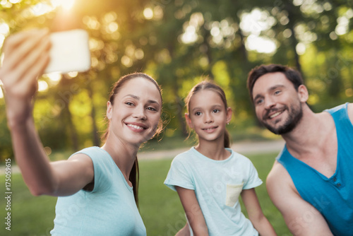 The family rests in the park after playing sports. A woman makes selfie with her family