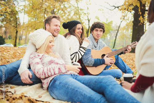  Friends having a good time in park at autumn/ singing and playing guitar 