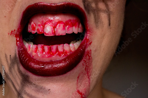 Closeup of Red lips of a young girl, with blood flowing by. Spooky woman smiling, mouth of woman in blood. Halloween or horror theme.