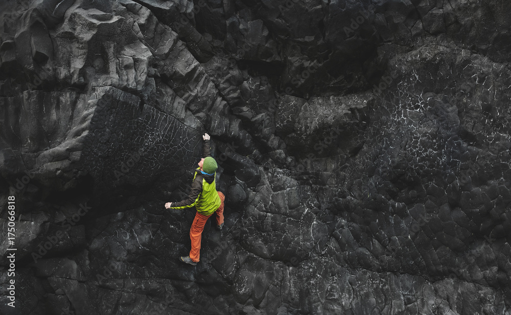Obraz premium male rock climber. rock climber climbs on a black rocky wall on the ocean bank in Iceland, Kirkjufjara beach. man makes hard move without rope.
