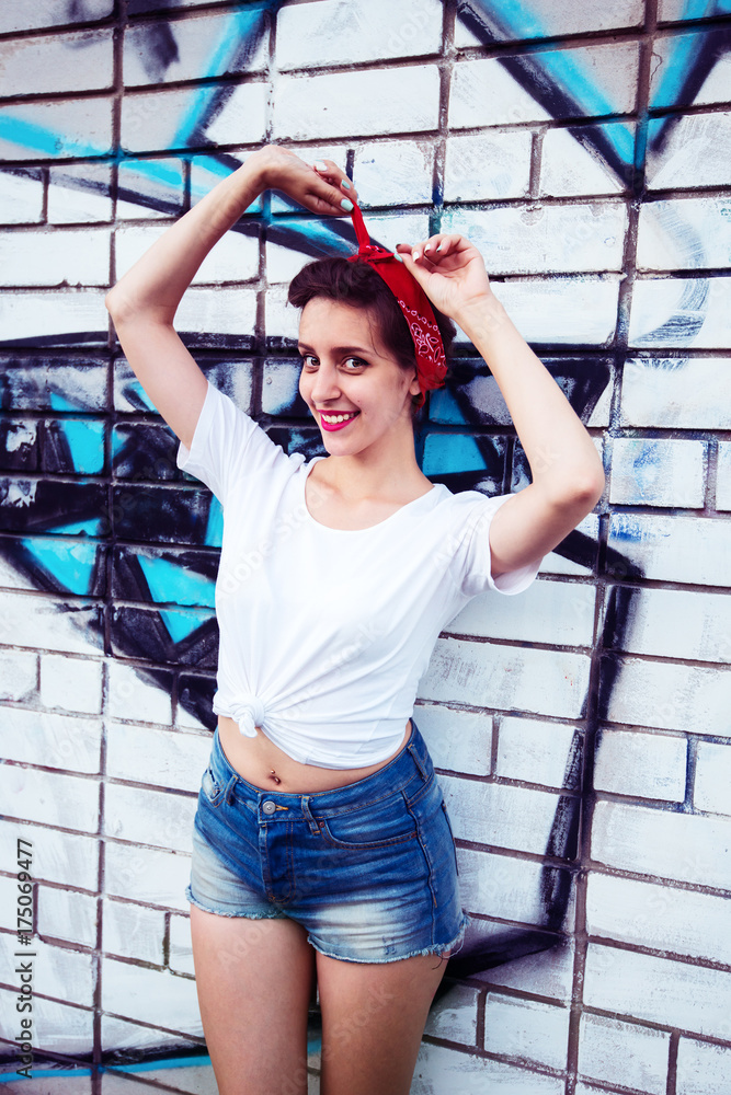 Joyful pin-up girl is posing next to a painted brick wall