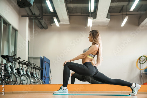 sporty slender young girl doing stretching legs in a light gym. Sport and health.