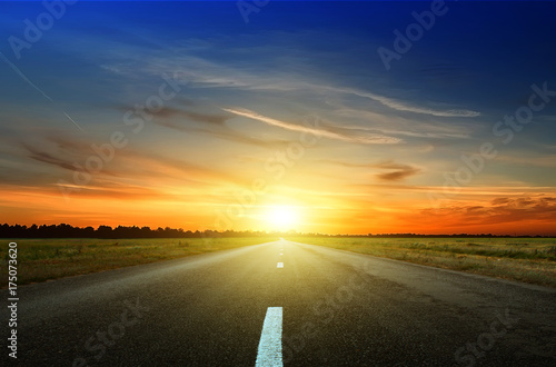 Asphalt road among the fields at sunset