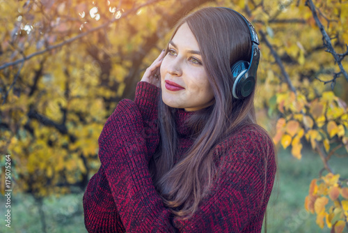 Woman in autumn Park standing listening to music with her headphones. Concept of good mood, favorite music, happy time. © Artem