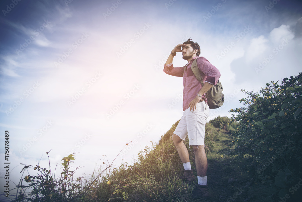 Young man standing on top of cliff in summer mountains at sunset and enjoying view of nature Young man standing on top of cliff in summer mountains at sunset and enjoying view of nature
