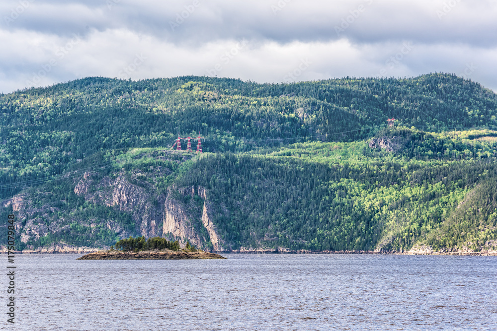 Fjord cliff coast in Saguenay river closeup of cliffs with power lines, wires and towers, tree forest, mountains and small island