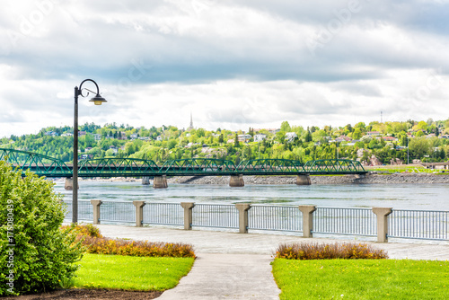 Sidewalk terrace wooden boardwalk in downtown city park in Saguenay, Canada, Quebec during summer with fjord river, bridge and railing fence, cityscape hills photo