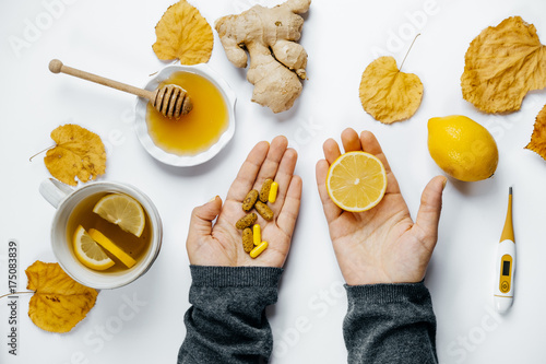 Woman hands with tablets and lemon, tea, thermometer, ginger, honey and dry leaves on a white background. flat lay