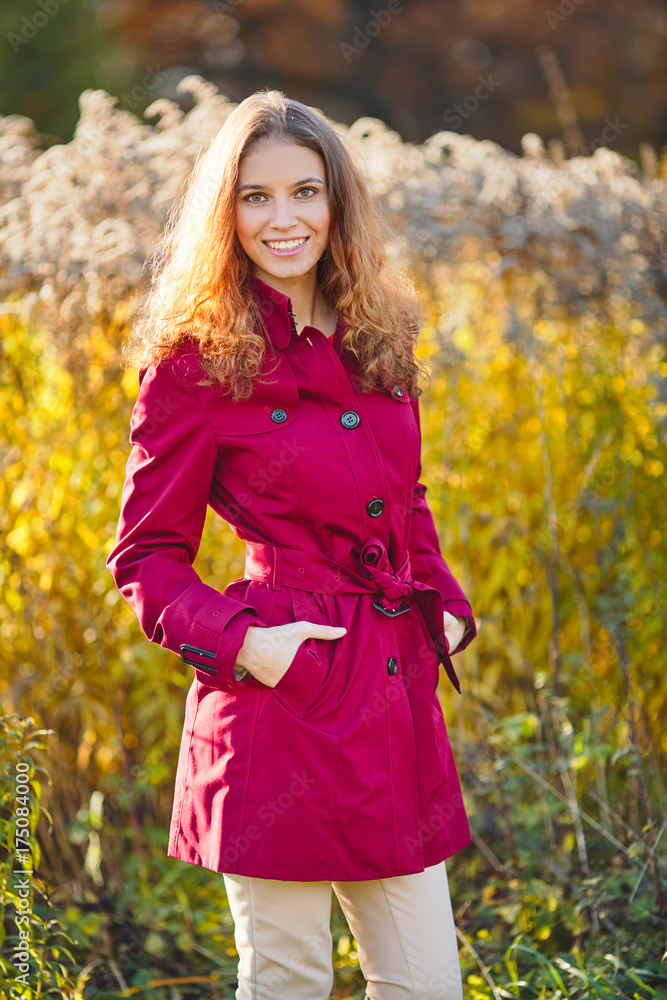 Beautiful young smiling woman in a red raincoat. Outdoor portrait in autumn park Beautiful young smiling woman in a red raincoat. Outdoor portrait in autumn park