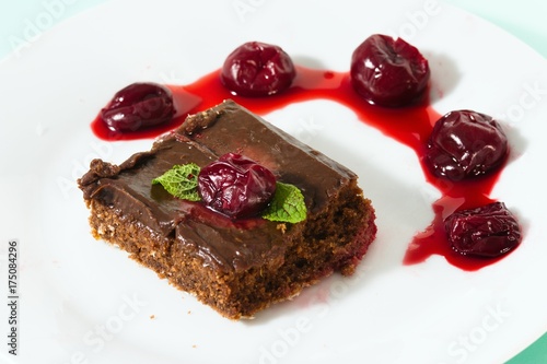 Square pieces of homemade brownie served on white plate with cherries and mint leafs