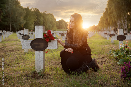 Sad woman in the cemetery, holding a bouquet of roses in her hand