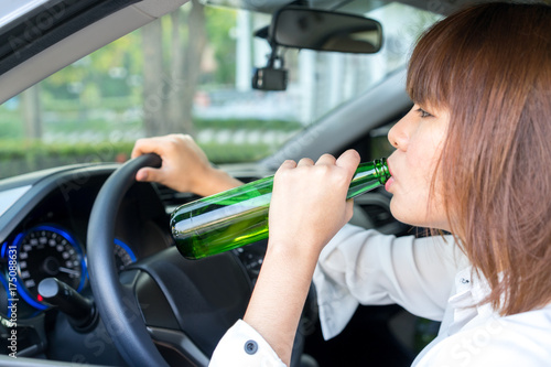 Drunk asian woman drinking alcohol and driving a car. © petzshadow